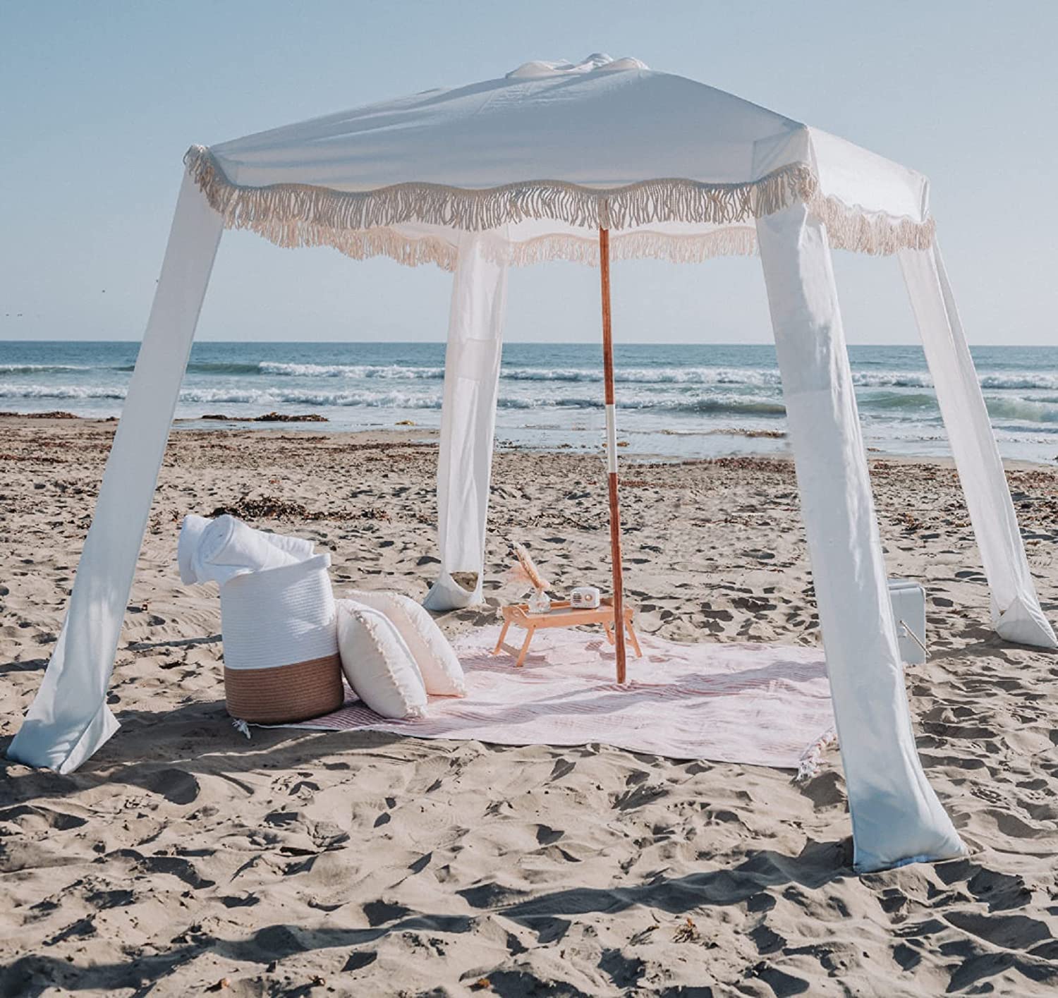 The AMMSUN Beach Cabana with Fringe, a stylish and functional beach shelter, set up on a sandy beach with a breathtaking ocean view, featuring a comfortable beach chair nearby.